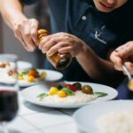 Chef cuisinier My Traiteur fait cuire des pates en polo noir brodé personnalisé